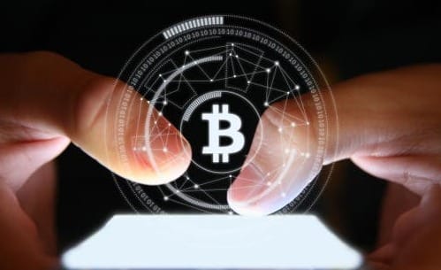 ضربة دولية تقضي على شبكة احتيال رقمي كبرى في دبي 3 شخص يستخدم هاتفاً ذكياً تظهر فوقه رسوم مضيئة لشعار عملة البيتكوين.